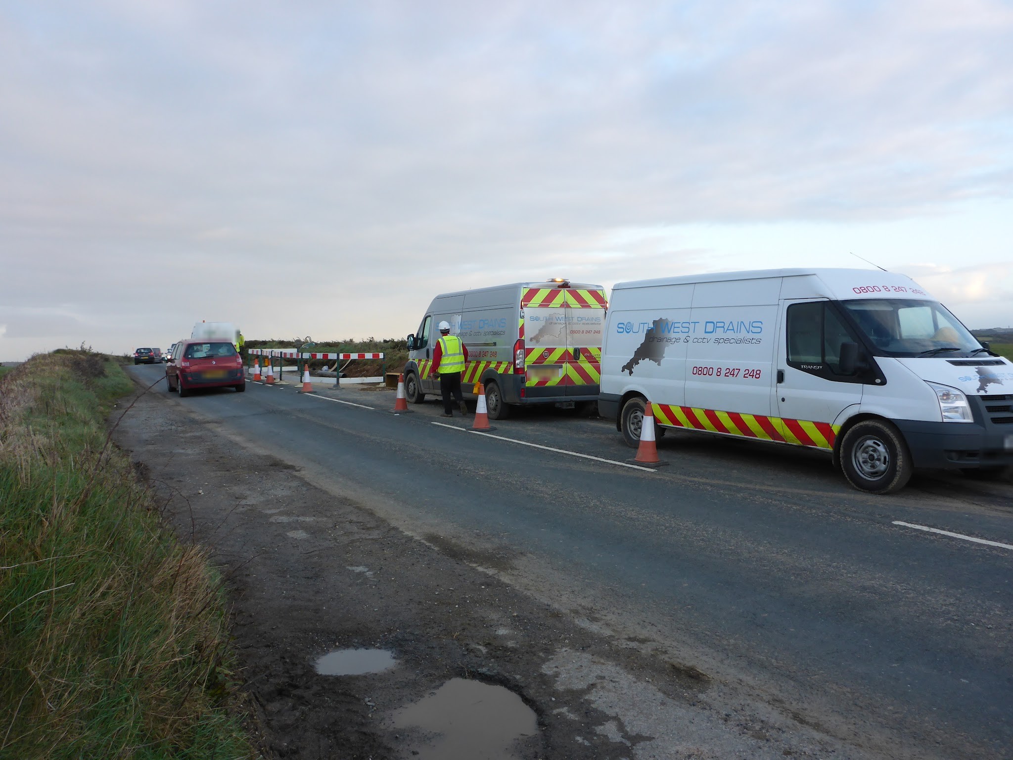 Two liveried South West Drains vans with cones on a rural road
