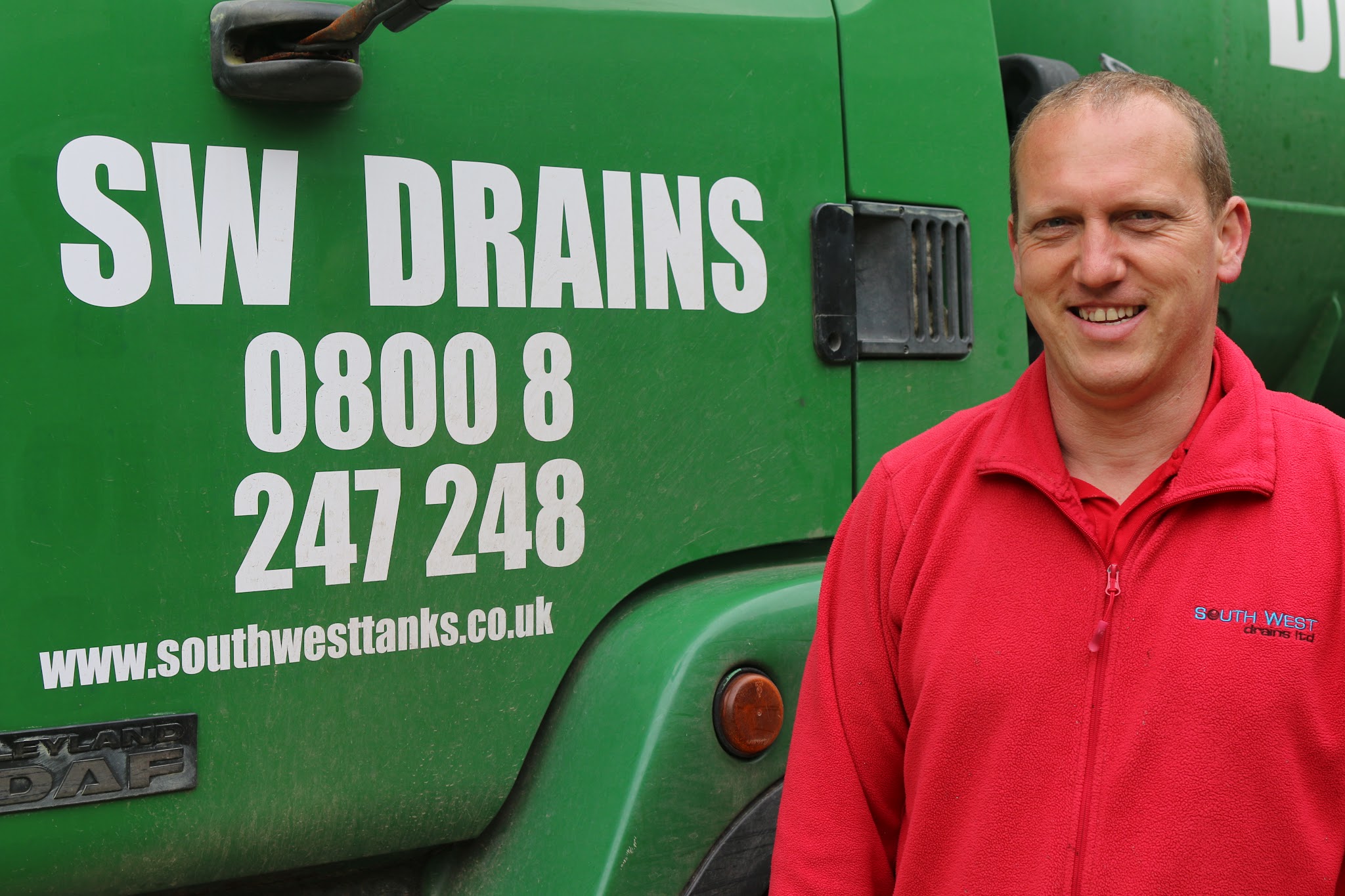 Jason in his red South West Drains fleece beside the green SW DRAINS tanker