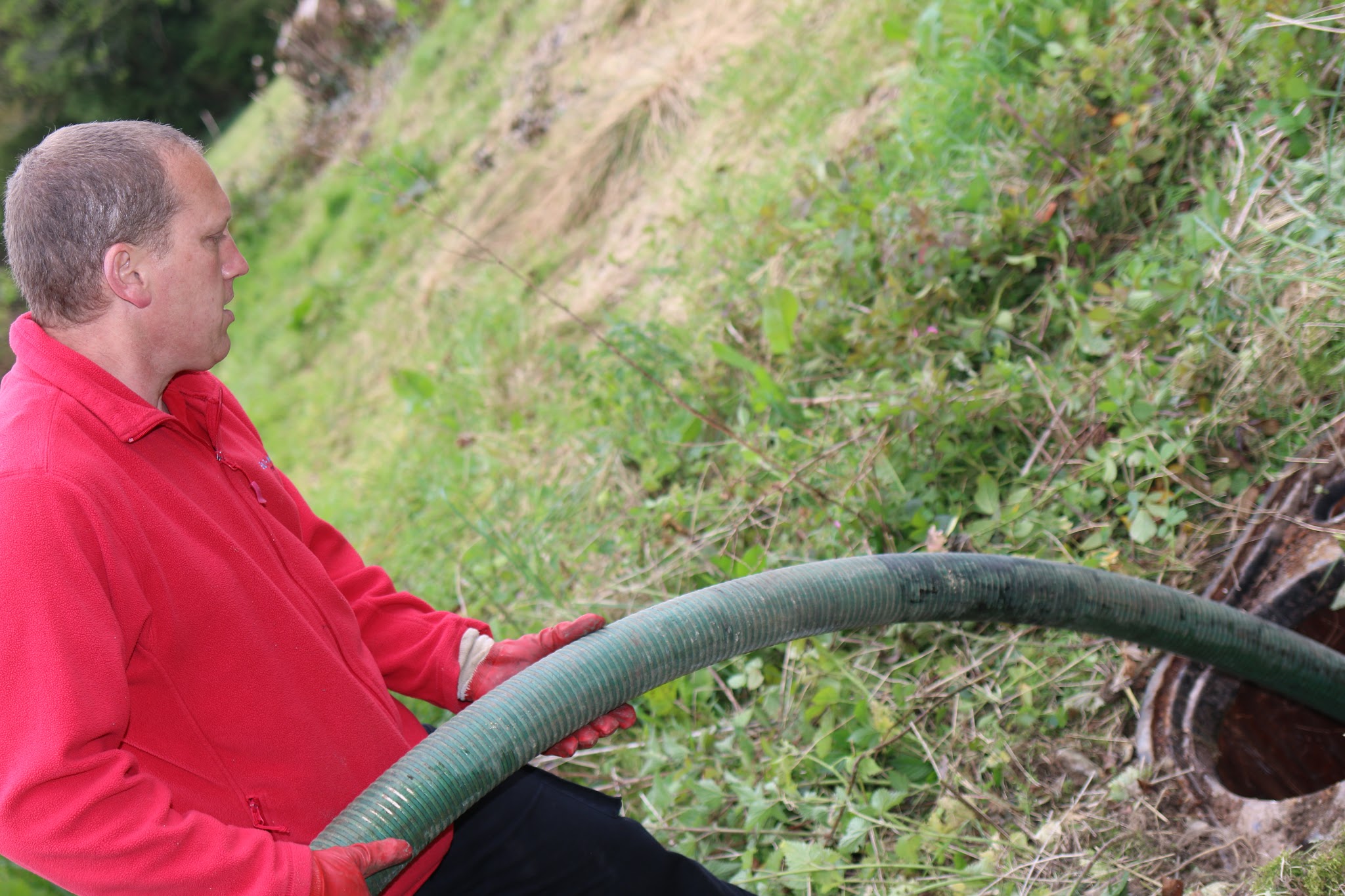 Jason holding the tanker suction hose on a grassy bank