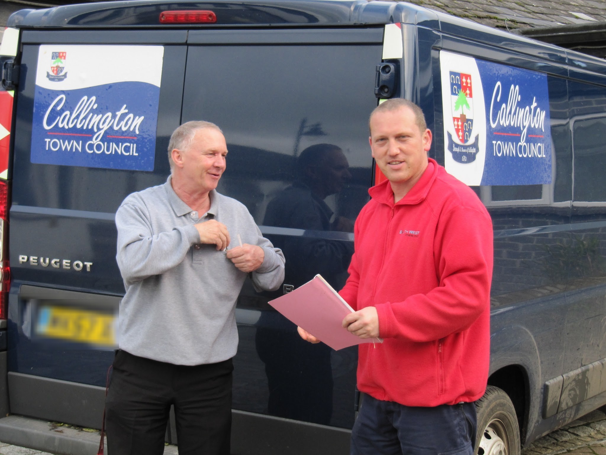 Jason shaking hands with a man beside a Callington Town Council van, holding a document