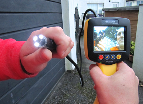 A handheld inspection camera with its screen showing the view inside a pipe