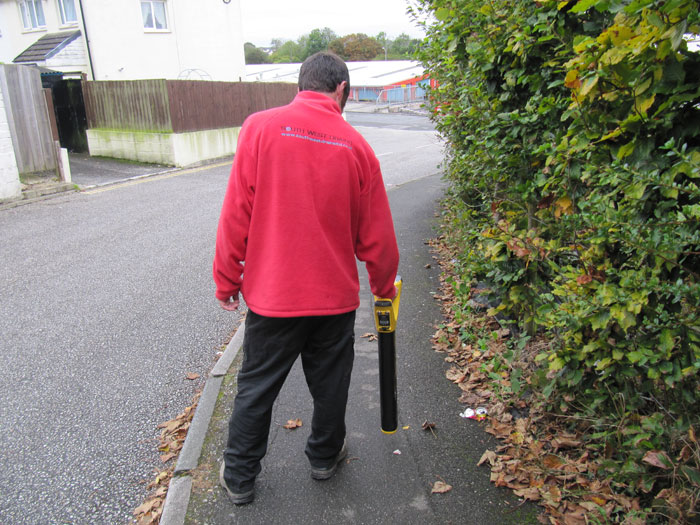 An engineer in a red South West Drains fleece walking a pavement with the locator