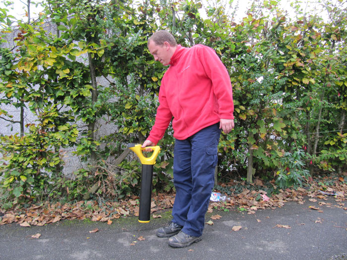Jason using a drain locator by a hedge