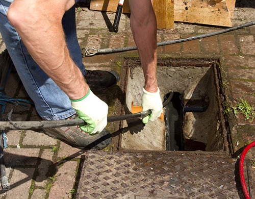 Gloved hands rodding an open manhole