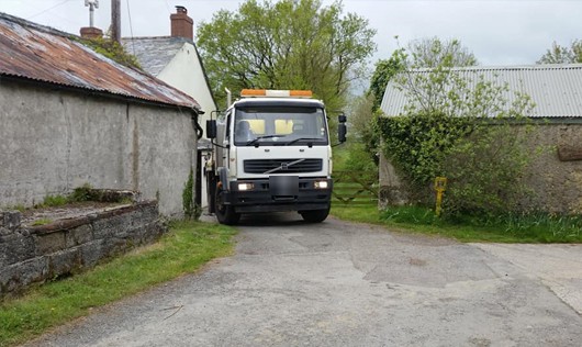 The yellow tanker in a farmyard lane between old stone buildings