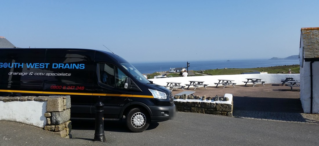 The navy South West Drains van on a cliff-top car park above the sea