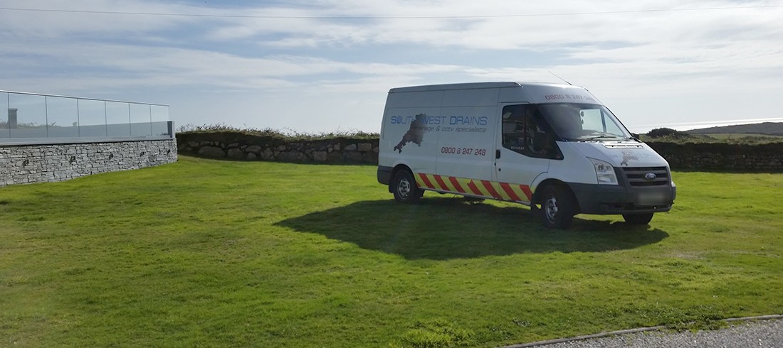 A white South West Drains van parked on grass by the coast